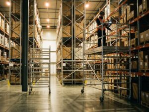 Magazijnmedewerker met handscanner op mobiele stelling tussen hoge opslag rekken in moderne warehouse