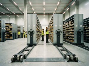 Moderne magazijnhal met mobiele stellingensystemen op rails die ruimte optimaliseren, werknemers tussen stalen rekken