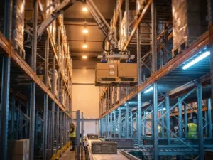 Geautomatiseerd magazijnstellingsysteem met robotarmen die pallets op hoge metalen rekken plaatsen onder industriële verlichting
